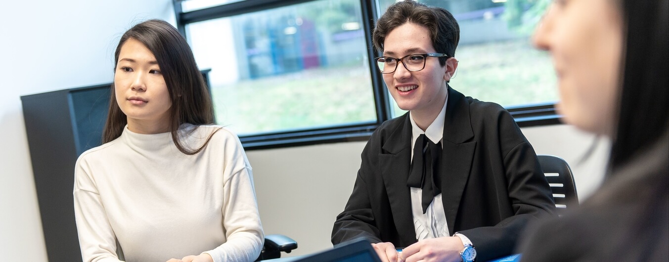Three students sit at a desk in interview attire.