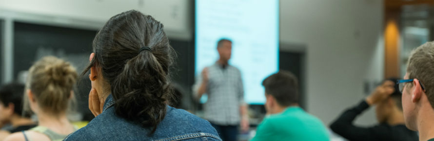 A prof lectures at the front of a classroom.