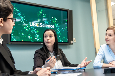 Three people sit at a table in a room chatting.