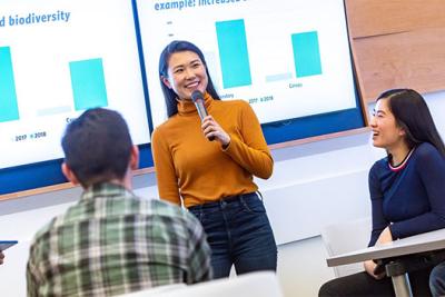 A person stands in front of a room presenting a powerpoint.
