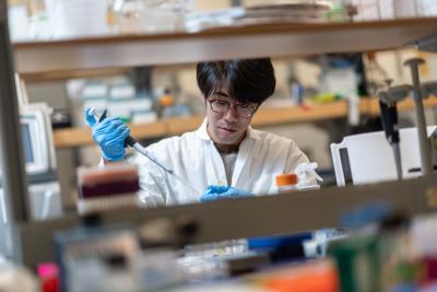 A student wearing a lab coat using a pipette.