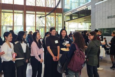 A group of students in the atrium of a building standing around and chatting.