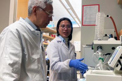 Two researchers wearing lab coats stand in a lab while looking at an experiment together.