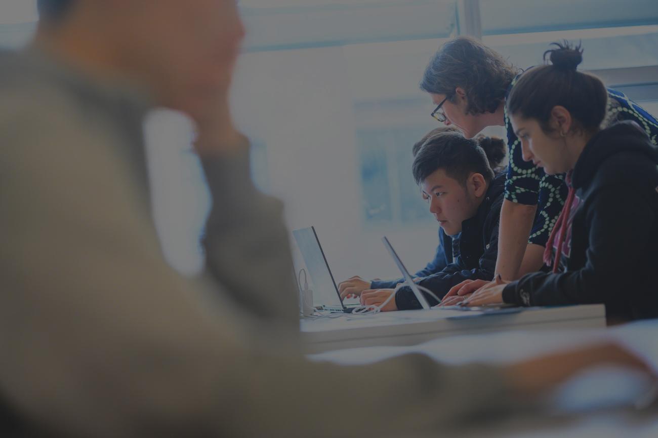 An instructor looks over two students at a desk