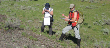 Two women wearing outdoor equipment stand in a field.