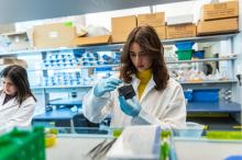 A student in a white lab coat examines specimen