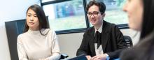 Three students sit at a desk in interview attire.