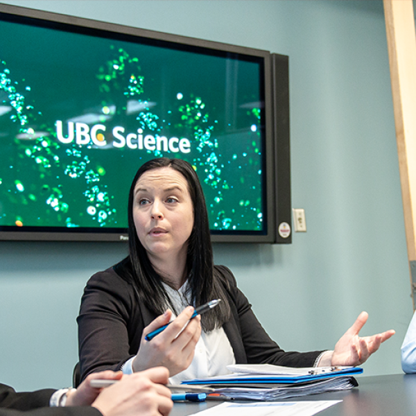 Three people sit at a table in a room chatting.