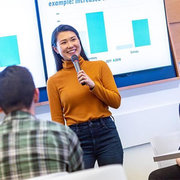 A person stands in front of a room presenting a powerpoint.